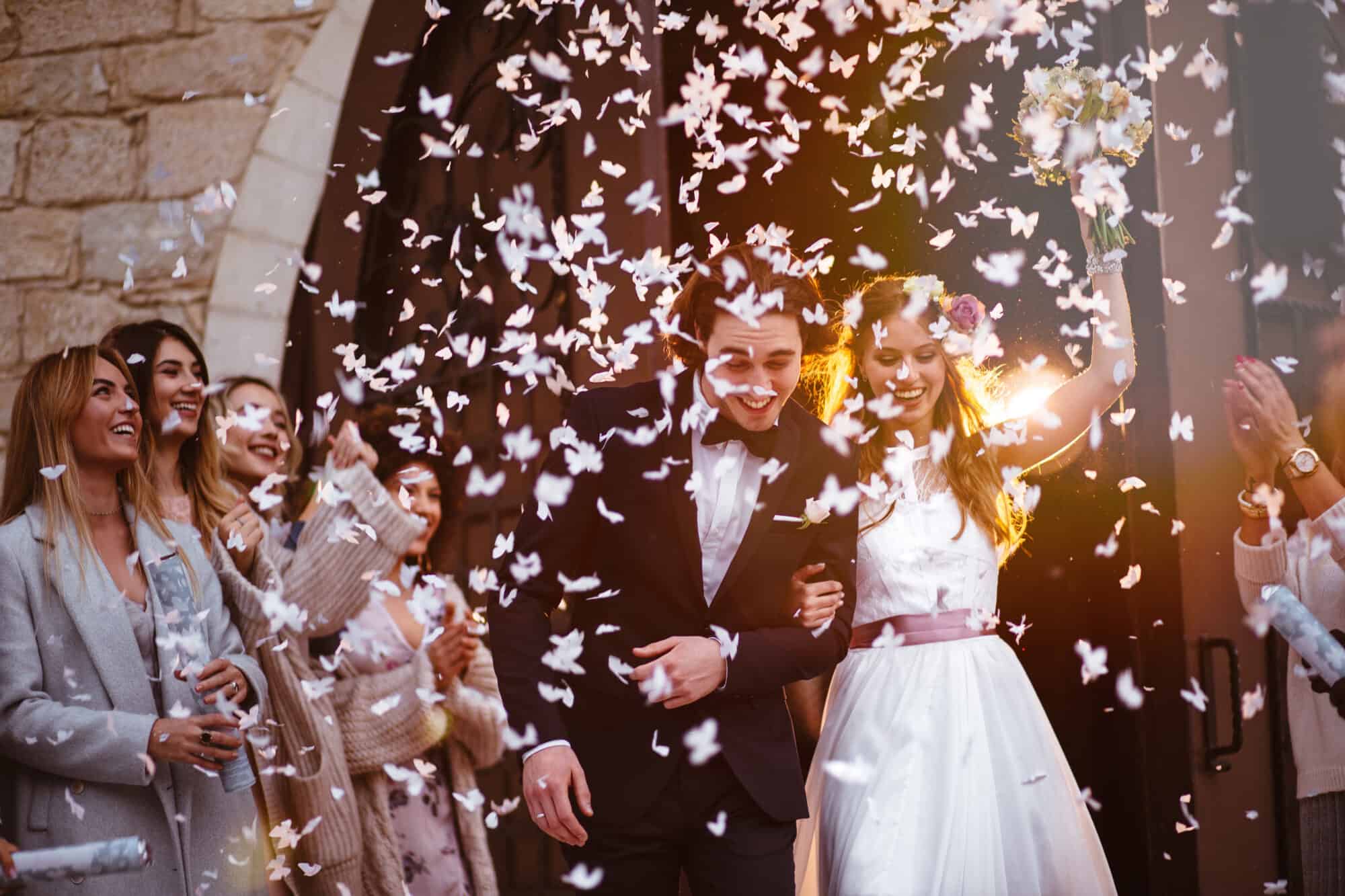 Newlywed husband and wife walking out of church and celebrating marriage with guests throwing confetti