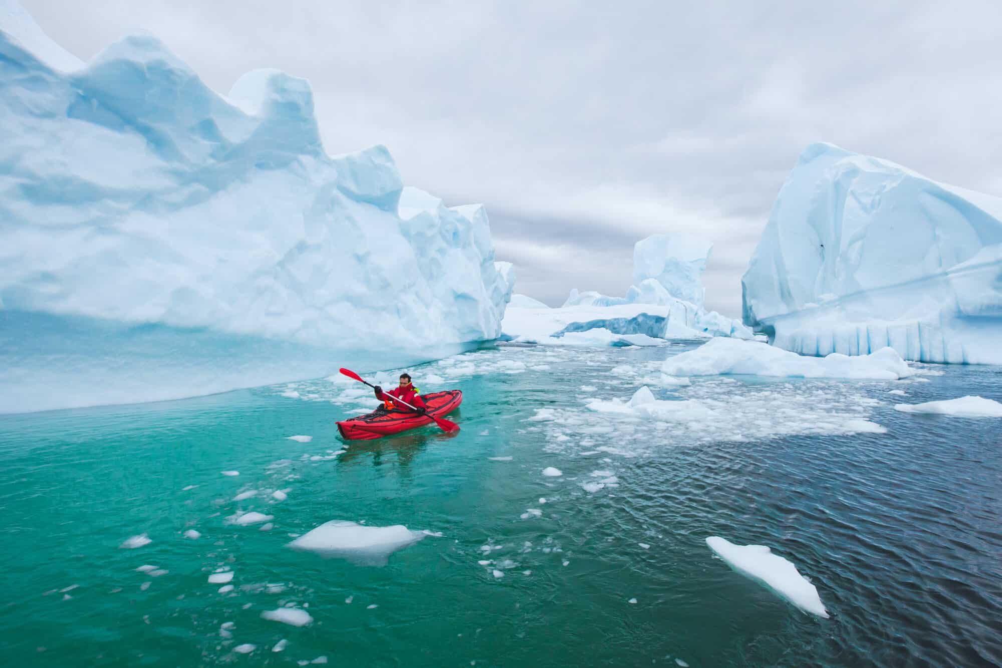 man paddling on kayak between ice in Antractica in Iceberg Graveyard, extreme winter kayaking, polar adventure near Pleneau island